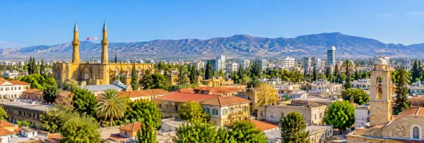 Panoramic view of Nicosia, Cyprus, featuring historic architecture, minarets, red-tiled roofs, and mountain scenery.