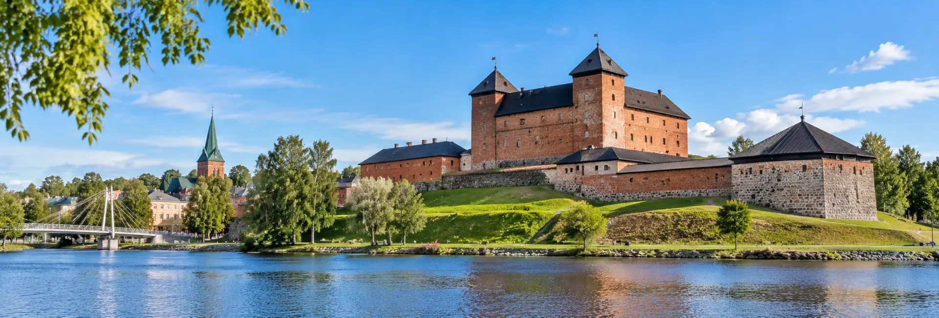Hämeenlinna Castle beside the waterfront with historic buildings and a church tower in Finland