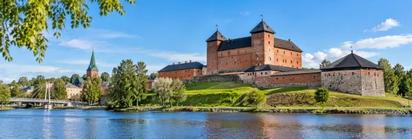 Hämeenlinna Castle beside the waterfront with historic buildings and a church tower in Finland