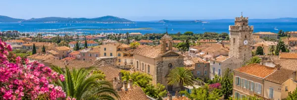 Hyères, France, with historic rooftops, palm trees, a stone tower, and Mediterranean coastline