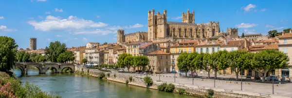 Narbonne, France, with historic rooftops, cathedral towers, and a scenic riverside promenade