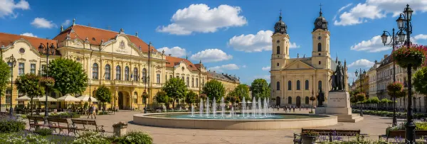 Historic city square in Békéscsaba, Hungary, with the Town Hall, church, fountain, and flower gardens.