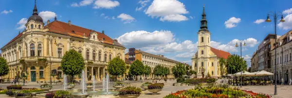 Kaposvár, Hungary, with historic buildings, a church tower, fountain, flowerbeds, and a lively central square.