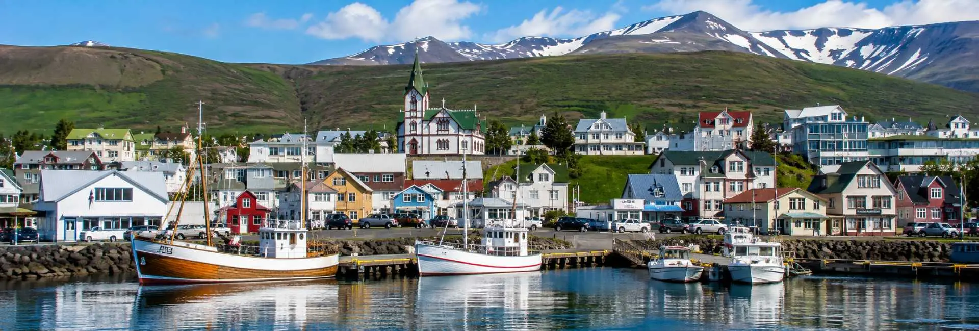 Húsavík, Iceland harbor with colorful houses, fishing boats, church, and snow-capped mountains