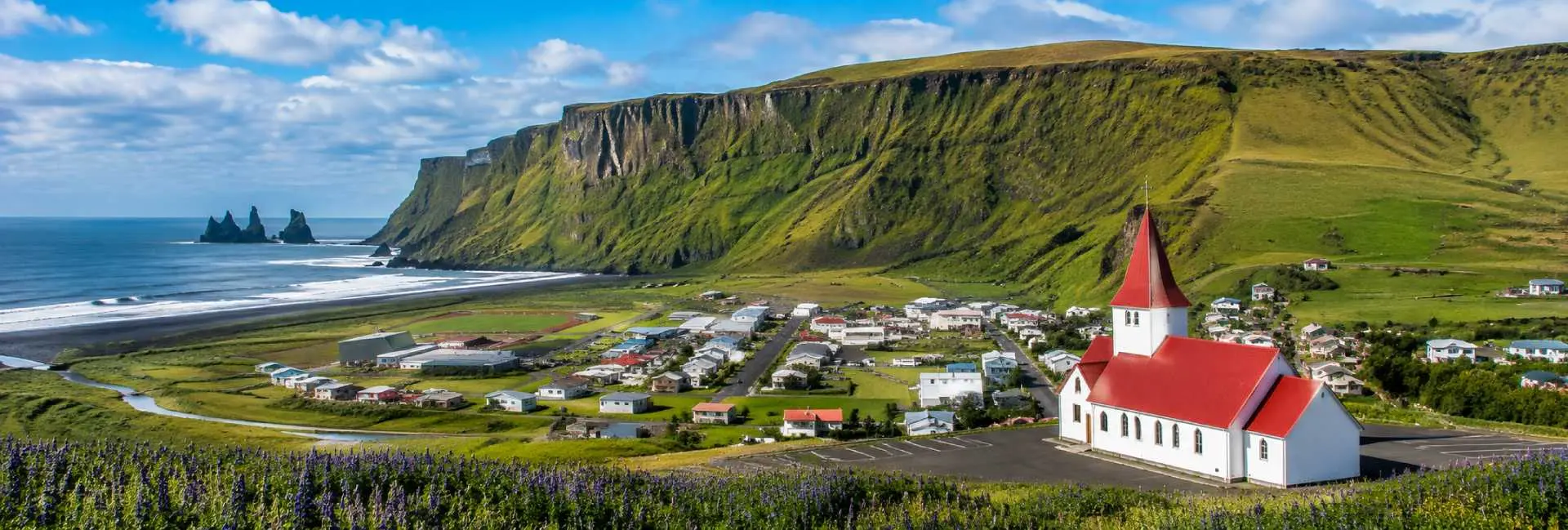 Vík, Iceland village with a red-roofed church, black-sand beach, cliffs, and sea stacks