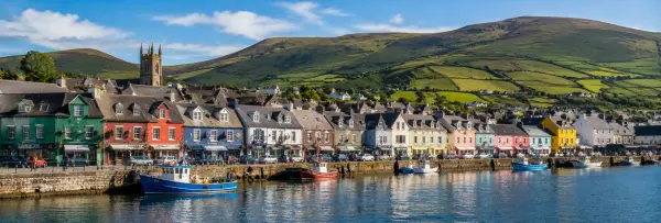 Colorful Dingle Harbour with fishing boats, historic buildings and green hills in Dingle, Ireland.