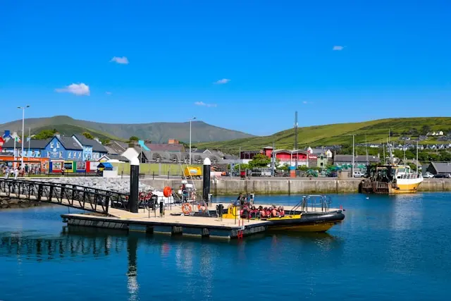Dingle Harbour with a small boat dock, colorful waterfront buildings, and green hills
