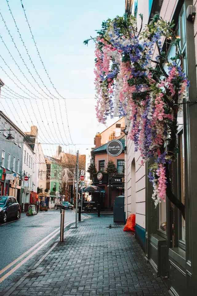 Colorful street in Galway City lined with shops, cafes, flower decorations, and traditional buildings