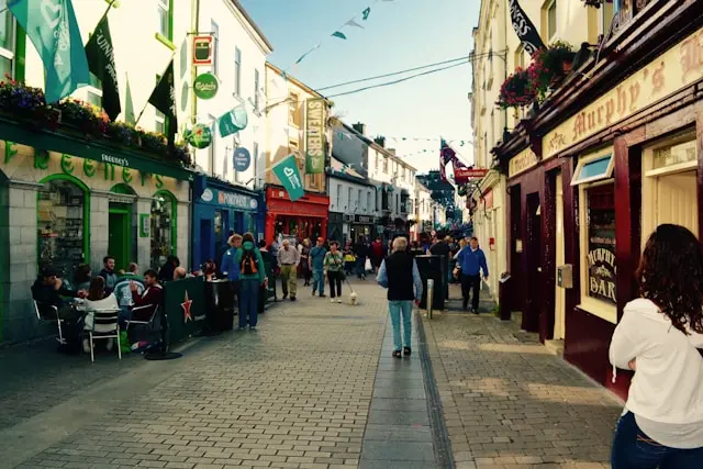 Busy pedestrian street in Galway City lined with colorful pubs, cafes, shops, and outdoor seating