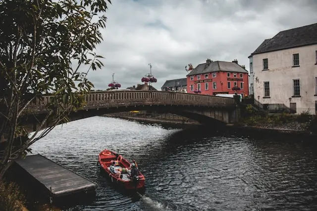 River flowing through Kilkenny with a stone bridge, colorful buildings, and a small boat