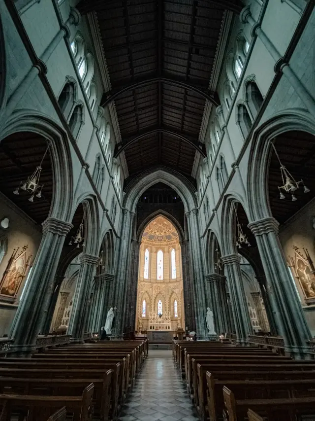 Interior of a historic Gothic church in Kilkenny with stone arches, wooden roof, stained glass windows, and rows of pews