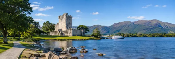 Ross Castle beside Lough Leane in Killarney, Ireland, with mountains and a scenic lakeside landscape.