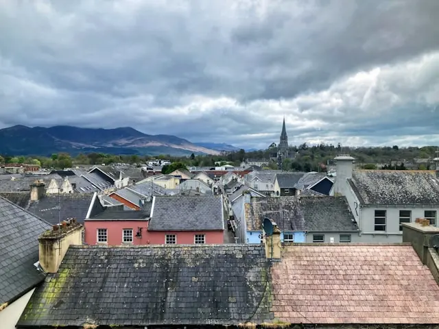 Rooftop view over Killarney with traditional buildings, a church spire, and mountains in the distance