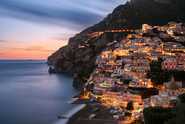Positano illuminated at dusk along the Amalfi Coast, with colorful houses overlooking the sea.
