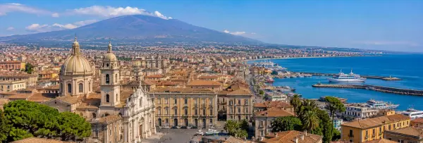 Panoramic view of Catania, Italy, with Mount Etna, historic buildings, harbor, and the Mediterranean Sea