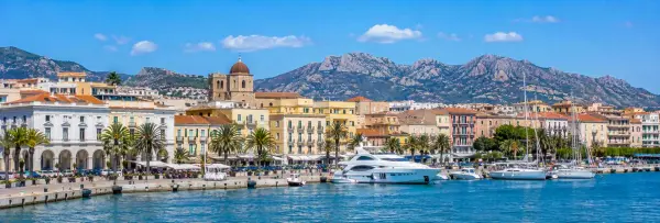 Olbia, Italy waterfront with colorful buildings, marina, palm trees and rugged Sardinian mountains