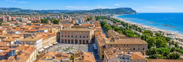Panoramic view of Pesaro, Italy, with Piazza del Popolo, historic rooftops, Adriatic beach and coastal hills.