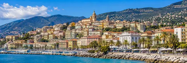 Sanremo, Italy coastal skyline with colorful buildings, palm-lined promenade, marina and mountain backdrop