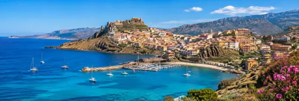 Sardinia coastal town with turquoise sea, marina, historic fortress and rugged Mediterranean mountains