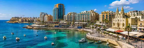 St. Julian's Malta waterfront with Spinola Bay, colorful boats, palm trees and historic church