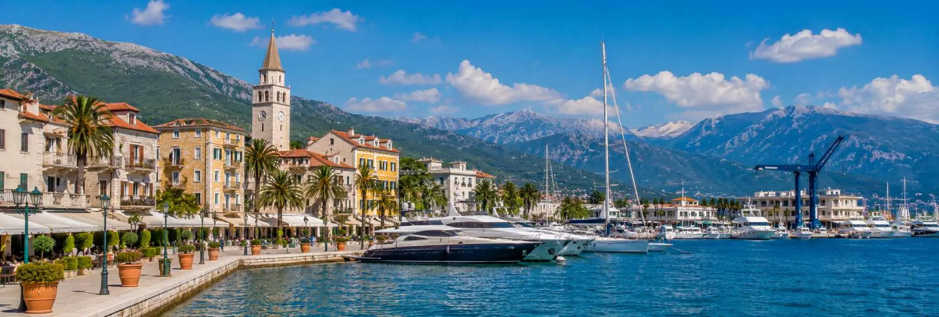 Tivat waterfront with luxury yachts, palm-lined promenade and dramatic mountains of the Bay of Kotor.