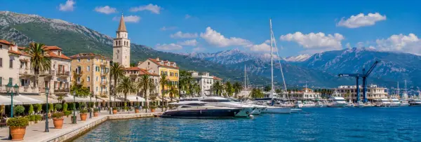 Tivat waterfront with luxury yachts, palm-lined promenade and dramatic mountains of the Bay of Kotor.