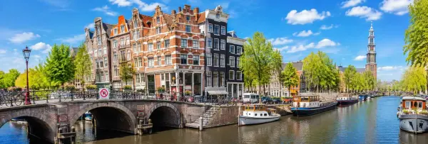 Panoramic view of Amsterdam featuring historic canal houses, bridges, boats, and scenic canals under a clear blue sky.