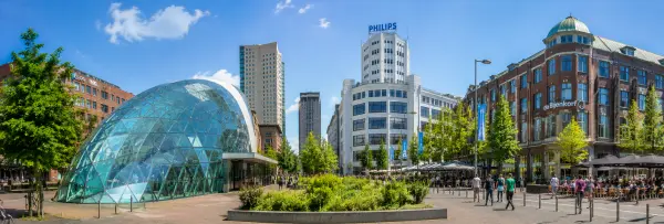 Modern Eindhoven cityscape with distinctive glass architecture, cafés, greenery, and lively streets.