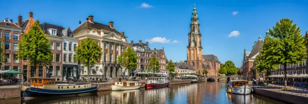 Historic Groningen canal with traditional Dutch buildings, boats, and the Martinitoren in daylight.