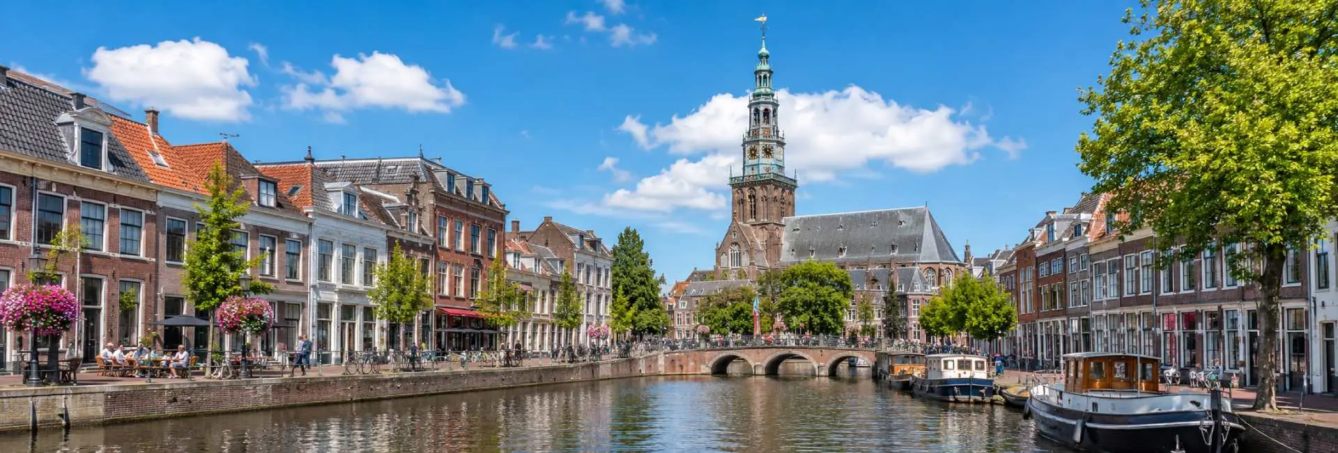 Leiden, Netherlands, with historic canal houses, boats, a bridge, and the city's church tower.