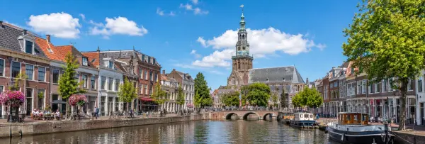 Leiden, Netherlands, with historic canal houses, boats, a bridge, and the city's church tower.