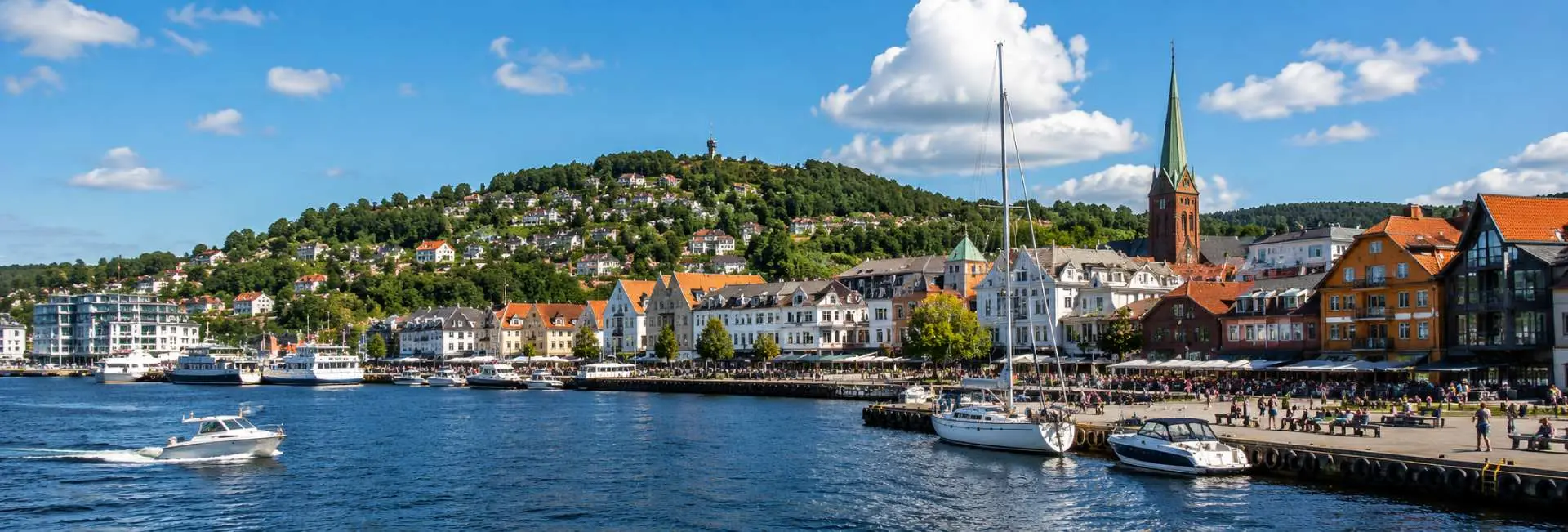 Kristiansand, Norway harbor with colorful waterfront buildings, boats, church spire and green hills