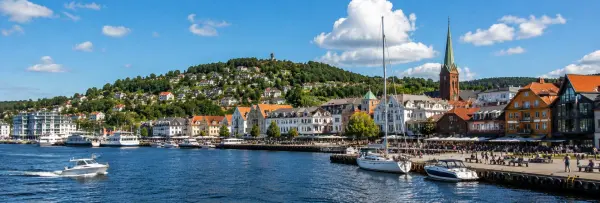Kristiansand, Norway harbor with colorful waterfront buildings, boats, church spire and green hills