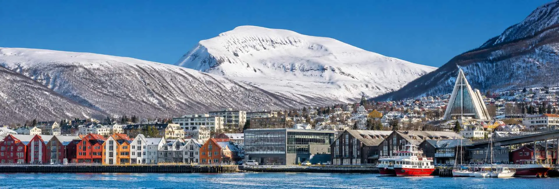 Tromsø, Norway waterfront with colorful buildings, Arctic Cathedral and snow-covered mountains