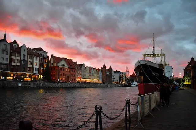Gdańsk waterfront at sunset with historic buildings and a docked boat along the Motława River