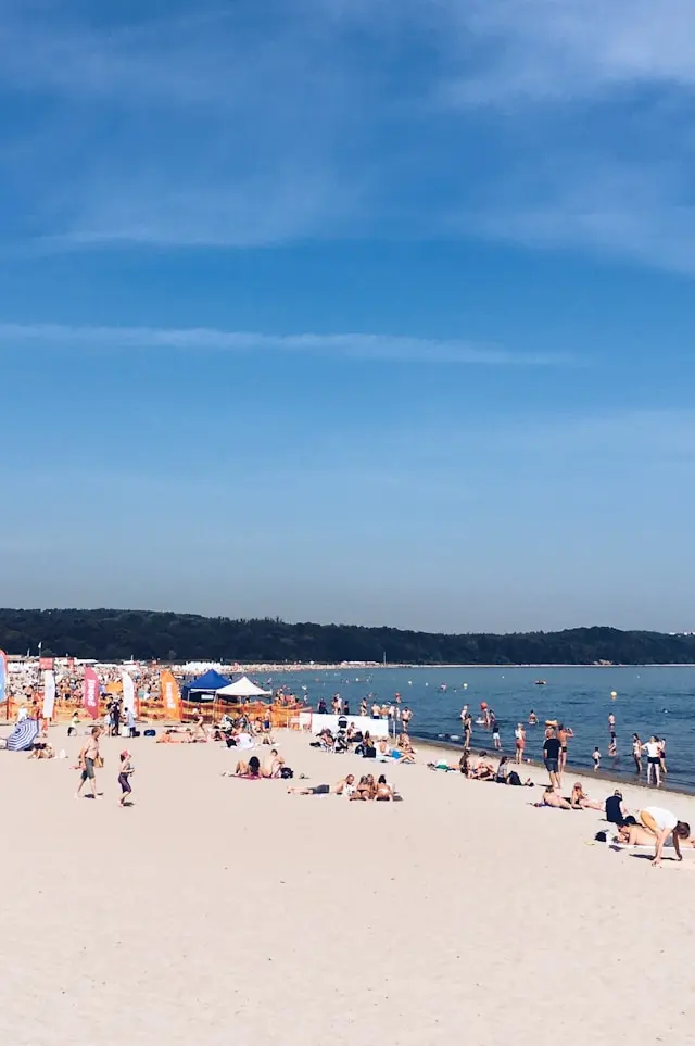 Crowded sandy beach with swimmers and visitors beside calm blue coastal waters