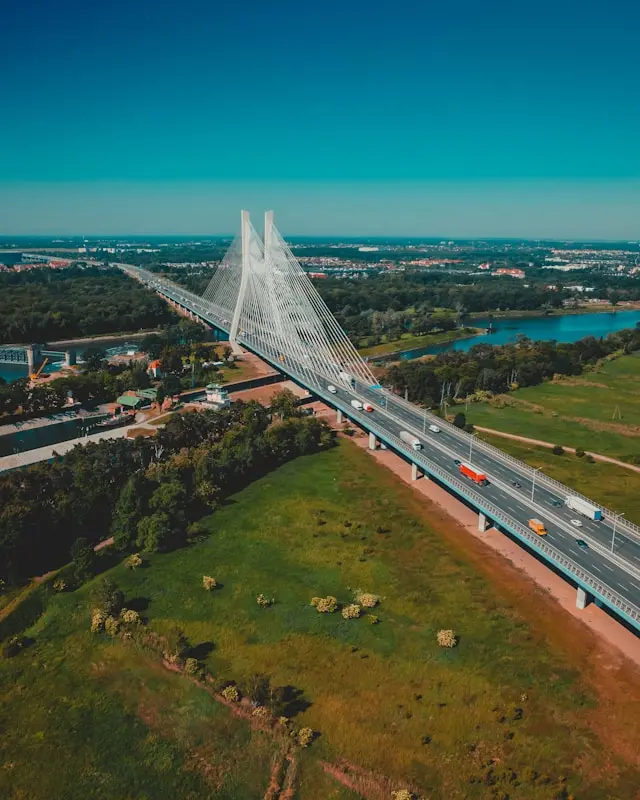 Aerial view of a modern cable-stayed bridge crossing a river surrounded by green parkland