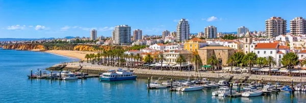 Portimão, Portugal, with its marina, palm-lined waterfront, sandy beach, and coastal cityscape.