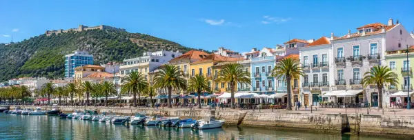Setúbal, Portugal waterfront with palm trees, colorful historic buildings, boats and hillside castle