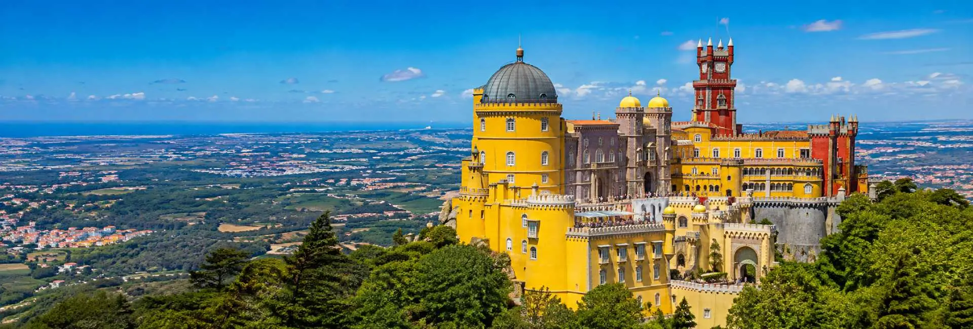 Pena Palace in Sintra, Portugal, surrounded by lush green hills under a bright blue sky