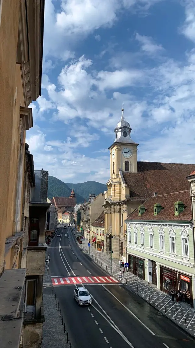 Historic street and clock tower in Brașov, Romania, with mountains in the background