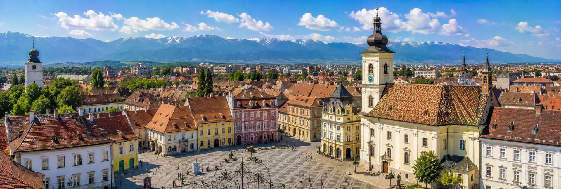Sibiu Grand Square with colorful historic buildings, Council Tower and Carpathian Mountains in Romania.