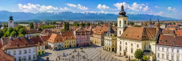 Sibiu Grand Square with colorful historic buildings, Council Tower and Carpathian Mountains in Romania.