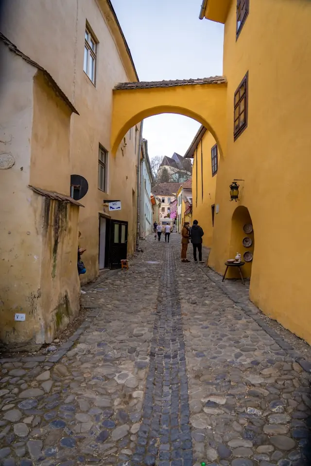Narrow cobblestone street with colorful historic buildings and an arched passage in Sighișoara, Romania