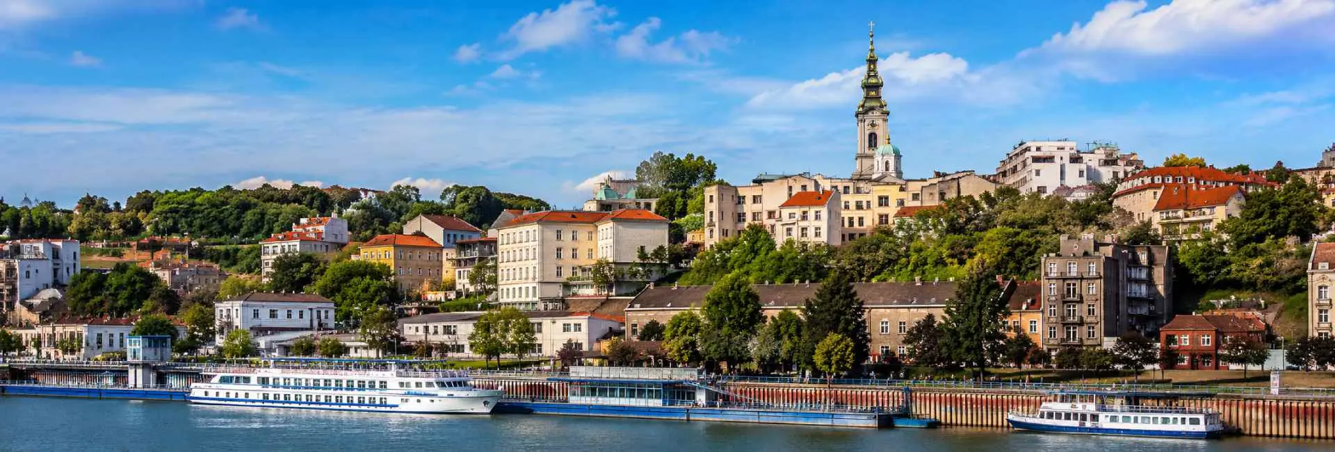 Belgrade Serbia cityscape with historic buildings, riverfront promenade and boats under a blue sky