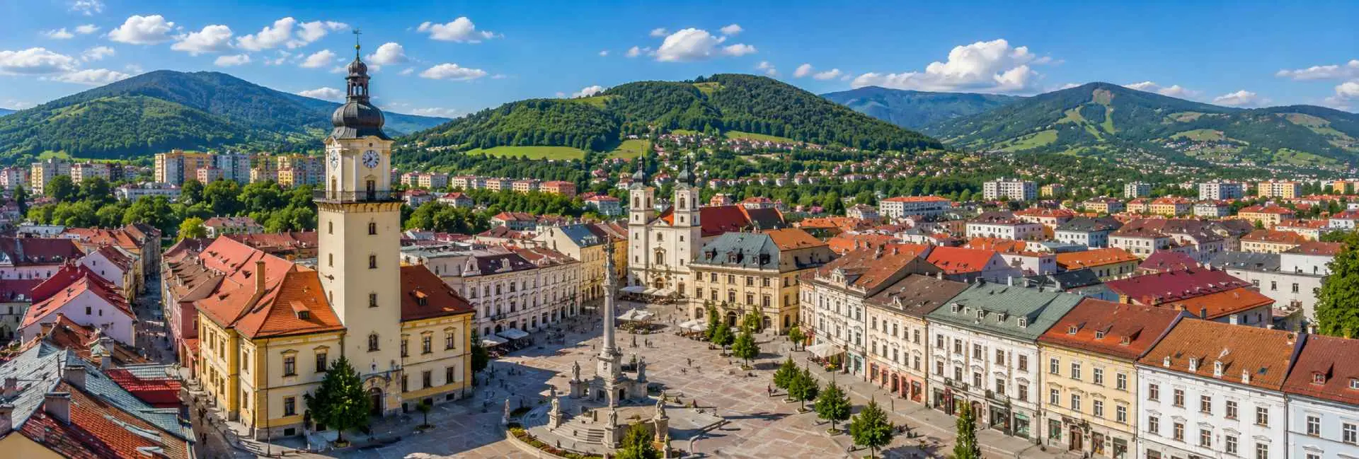 Banská Bystrica, Slovakia, with its historic square, clock tower, churches and surrounding green mountains.