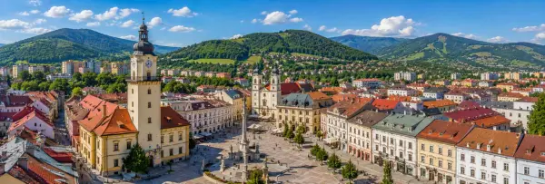 Banská Bystrica, Slovakia, with its historic square, clock tower, churches and surrounding green mountains.