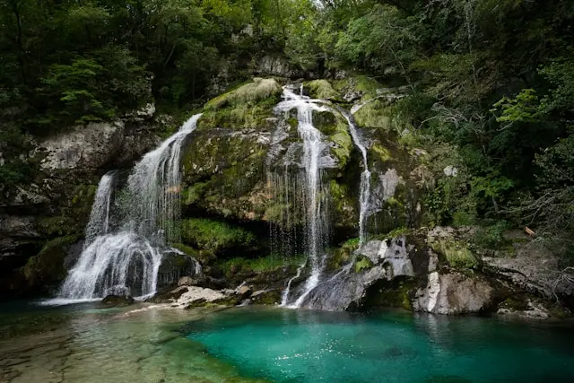 Waterfall and turquoise pool surrounded by forest in Bovec, Slovenia