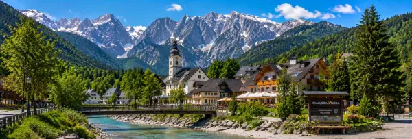 Kranjska Gora village with alpine chalets, church, green forests and dramatic Julian Alps in Slovenia.