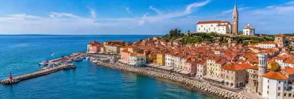 Piran waterfront with colorful Venetian buildings, Adriatic Sea and St. George's Church in Slovenia.